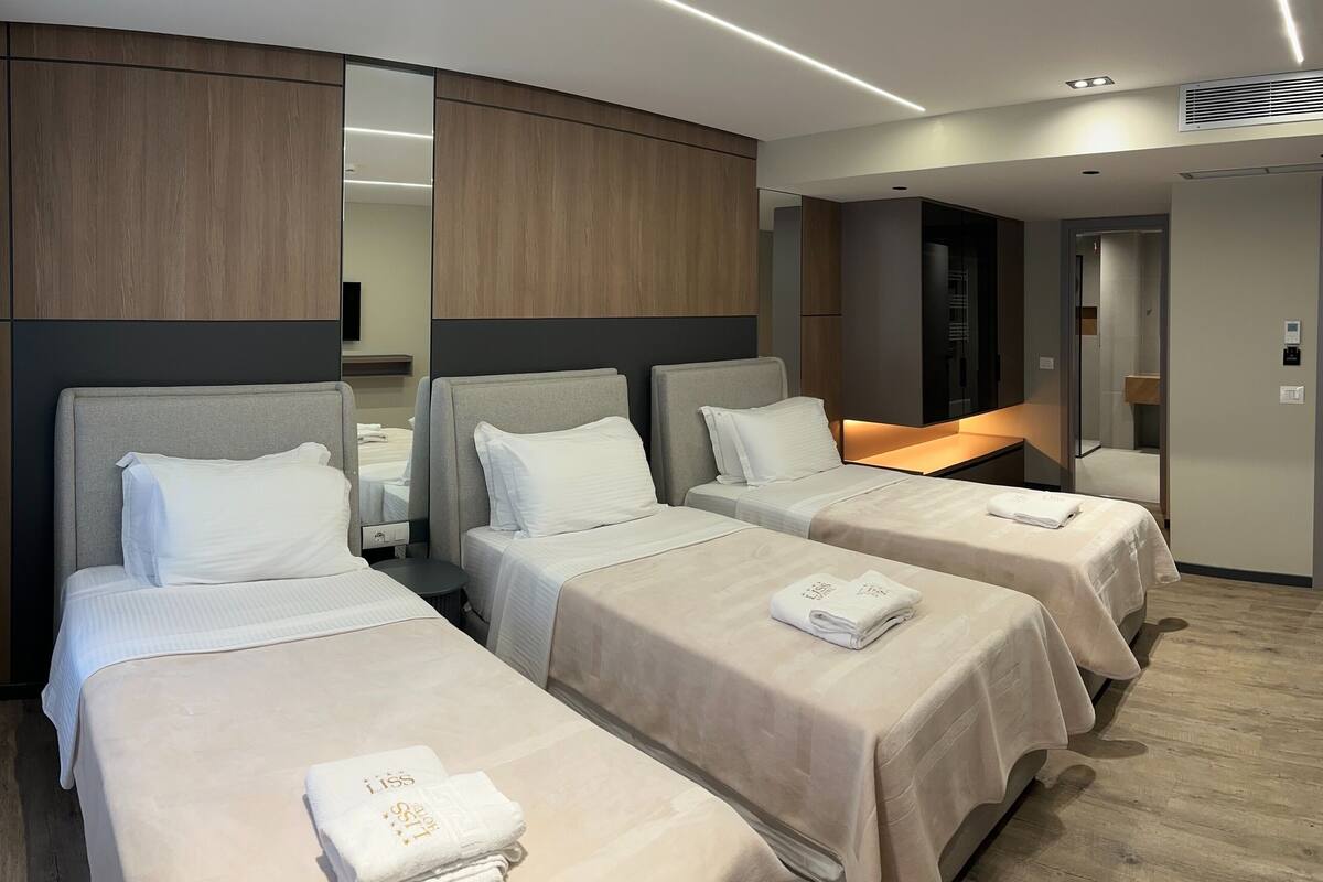 A hotel room with three beds, a mirror, a bedside table, and a modern design.
