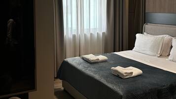 Habitación de hotel con cama, cortinas, cabecero, televisor de pantalla plana y suelo de madera.