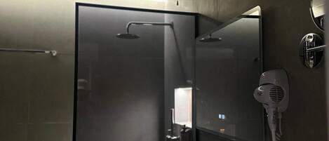 Un baño moderno con cabina de ducha de vidrio, un lavamanos blanco y un secador de pelo fijado a la pared.