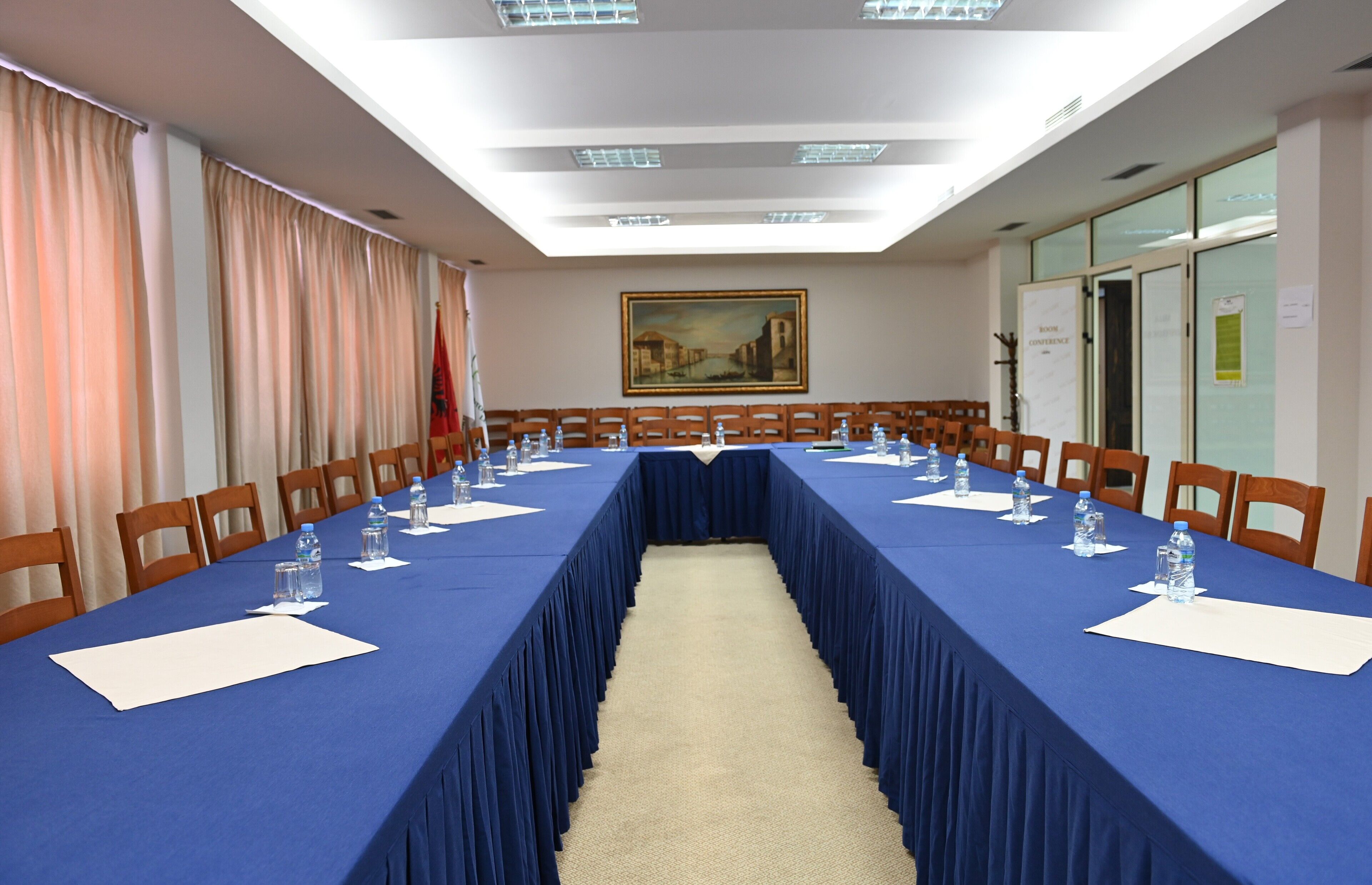 A conference room with a long table, chairs, water bottles, and a painting on the wall.