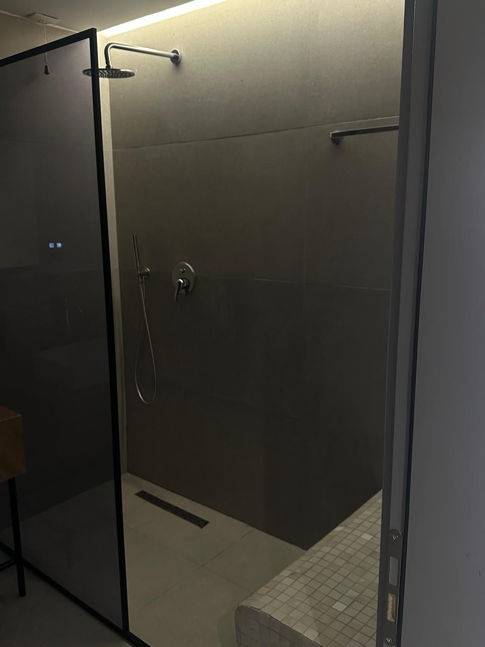 Une cabine de douche moderne dotée d’une porte en verre, d’un pommeau de douche à main et d’un robinet mural.
