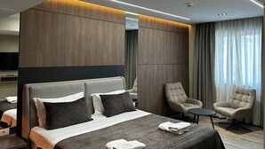 A modern hotel room with a large bed, two armchairs, a small table, and a television. - Hotel Liss (Lezhe)