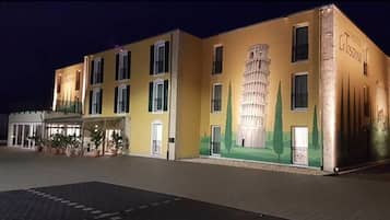 Ein Hotel mit einer auffälligen Wandmalerei eines schiefen Turms, einem befestigten Eingangsbereich und einer gut beleuchteten Fassade.