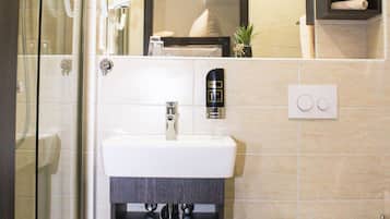 Un baño moderno con cabina de ducha de vidrio, un lavamanos blanco con mueble oscuro debajo, un inodoro y una pequeña planta en maceta en la pared.