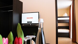 A room with a TV displaying "WELCOME" on the screen, a bunk bed, a bottle, and a glass with a card. - Hotel La Toscana Nähe Europapark  mit Ticket Garantie (Ringsheim)