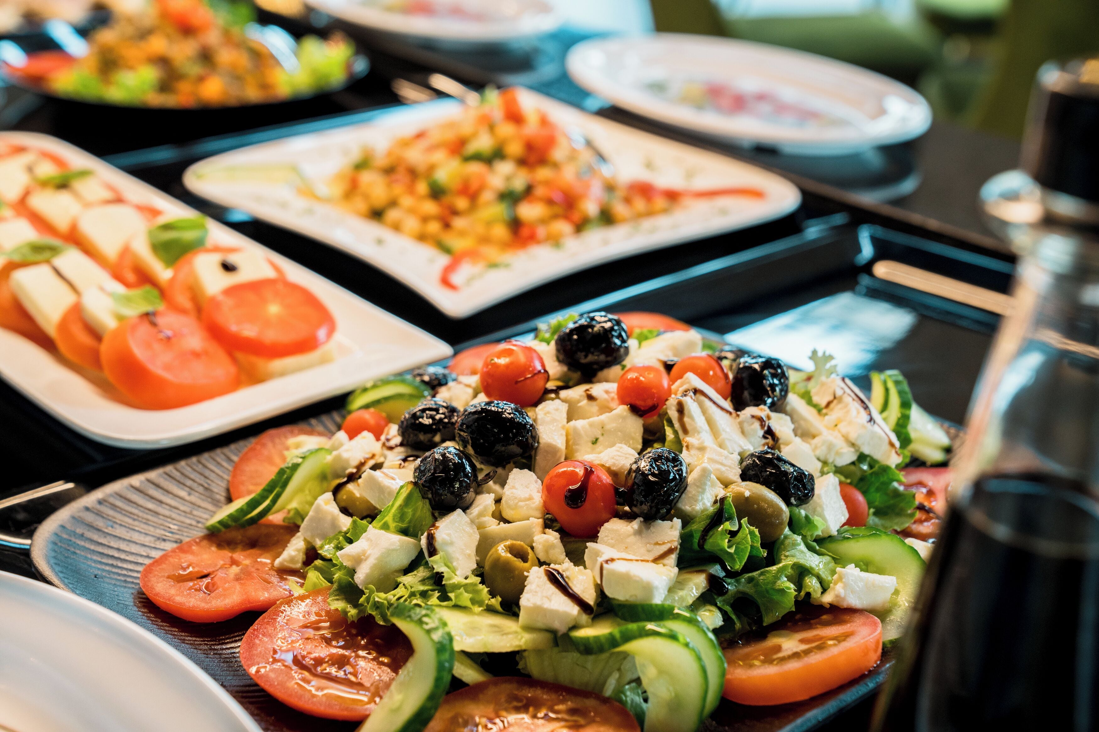 A buffet with various dishes including a salad with tomatoes, cucumbers, and olives.