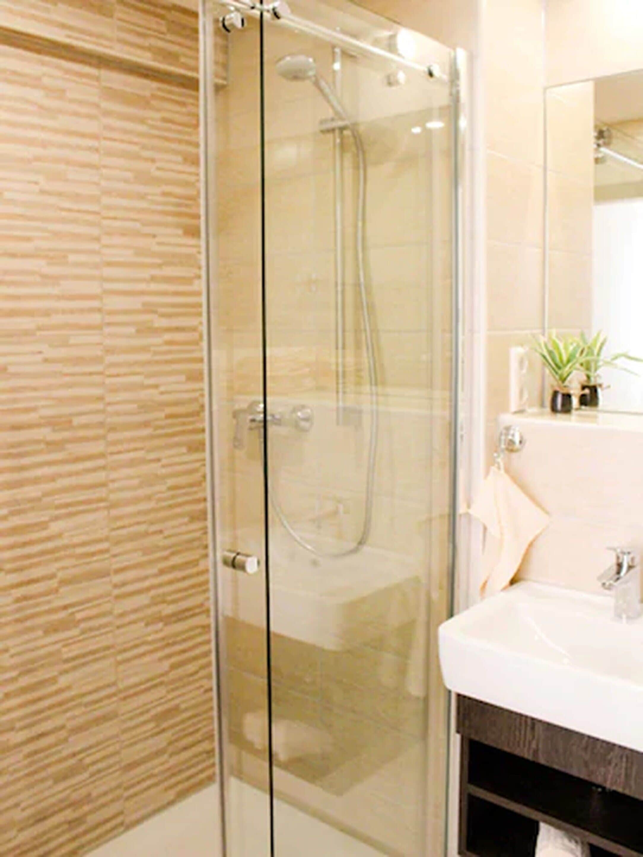 A modern bathroom with a glass shower enclosure, a white sink, and a mirror above it.