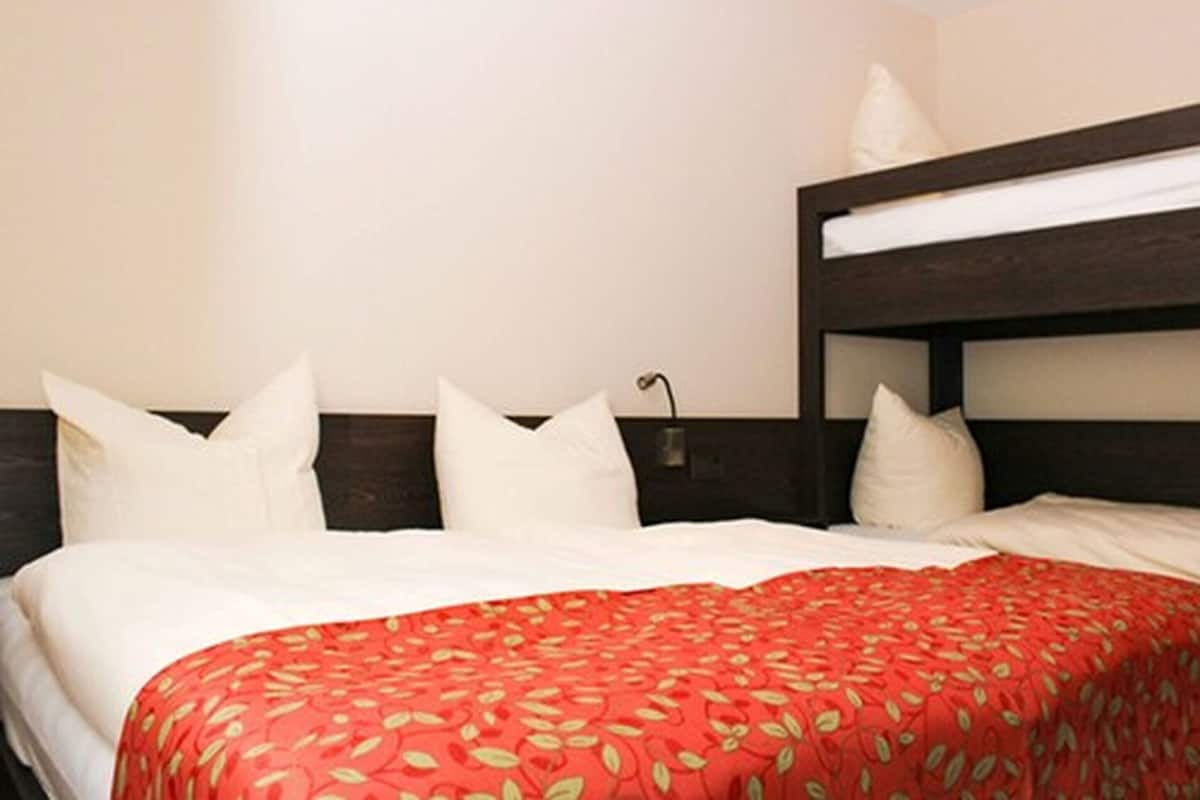 A hotel room with a bunk bed, white bedding, and a red floral bedspread.