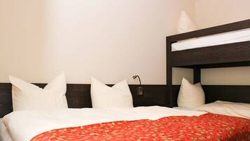 Una habitación de hotel con literas, ropa de cama blanca y una colcha de flores rojas.