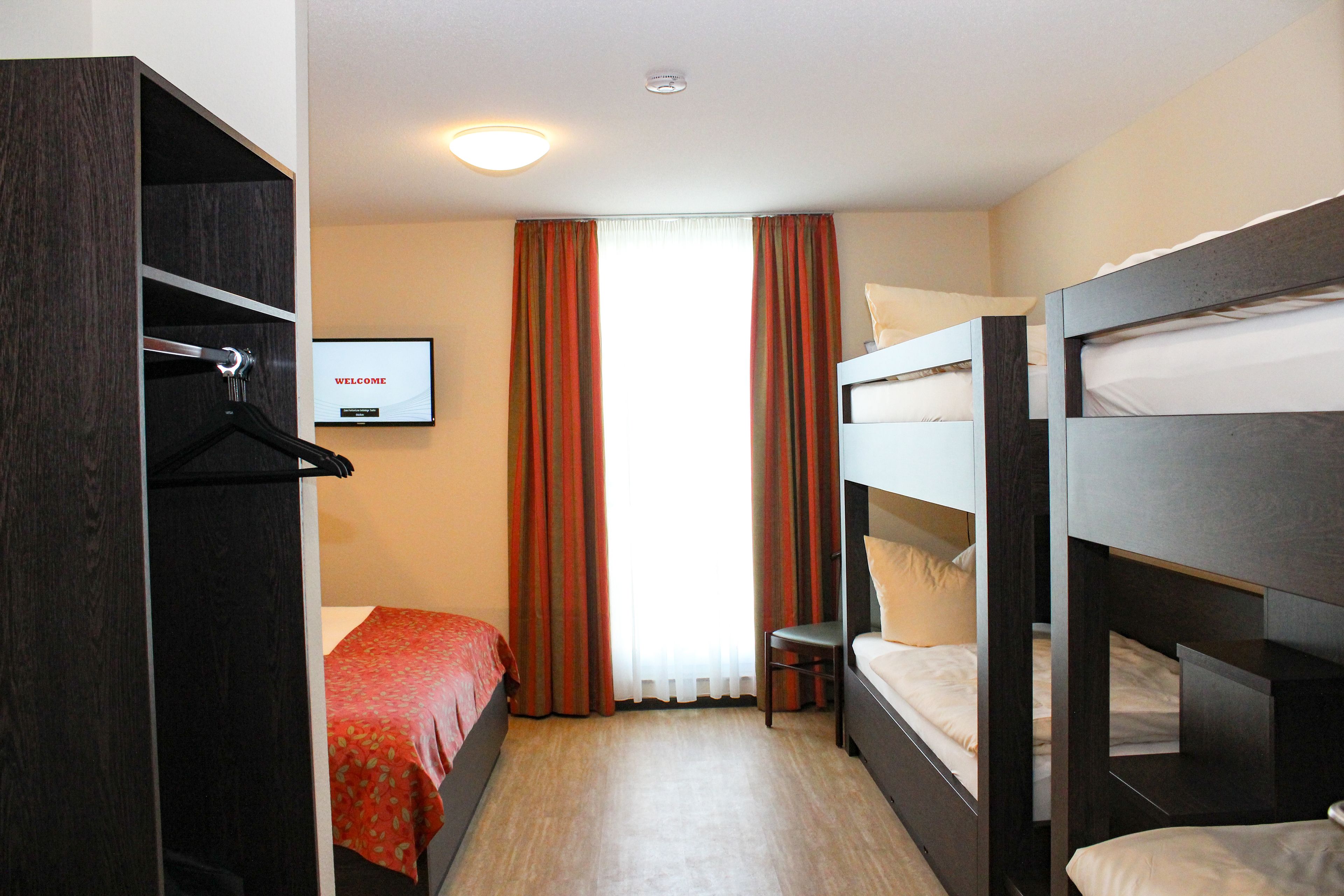 A hotel room with bunk beds, a wooden wardrobe, a television, and a window with curtains.