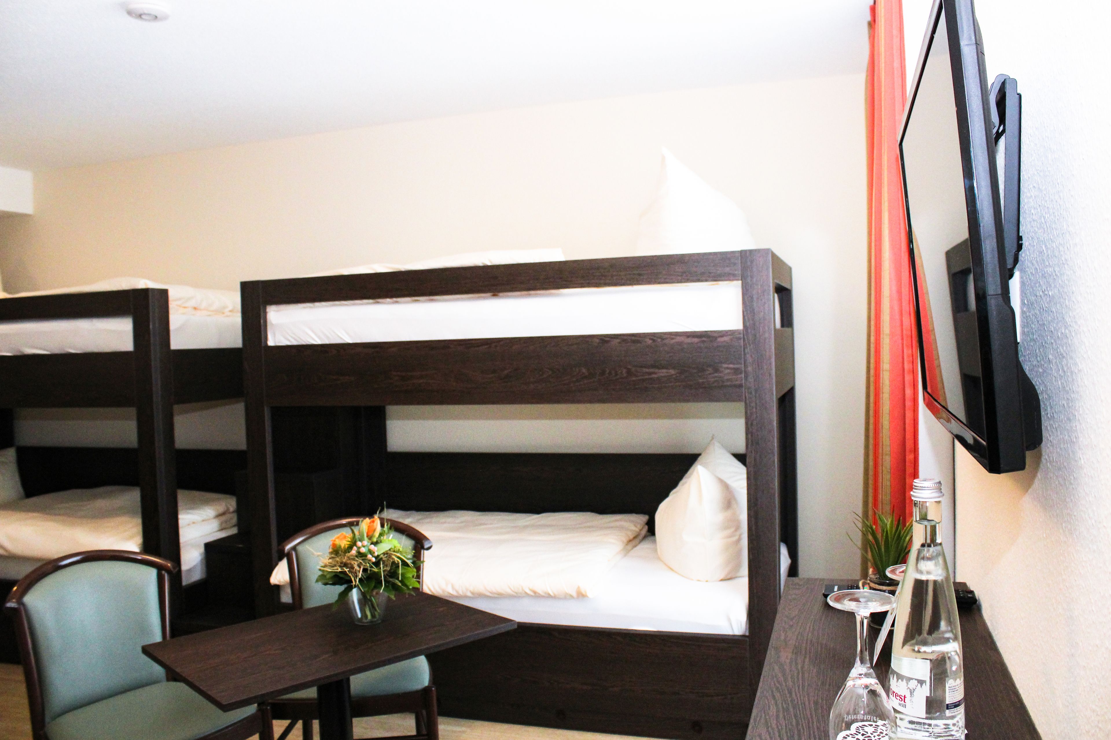 A hotel room with bunk beds, a small table with a vase, and a TV mounted on the wall.