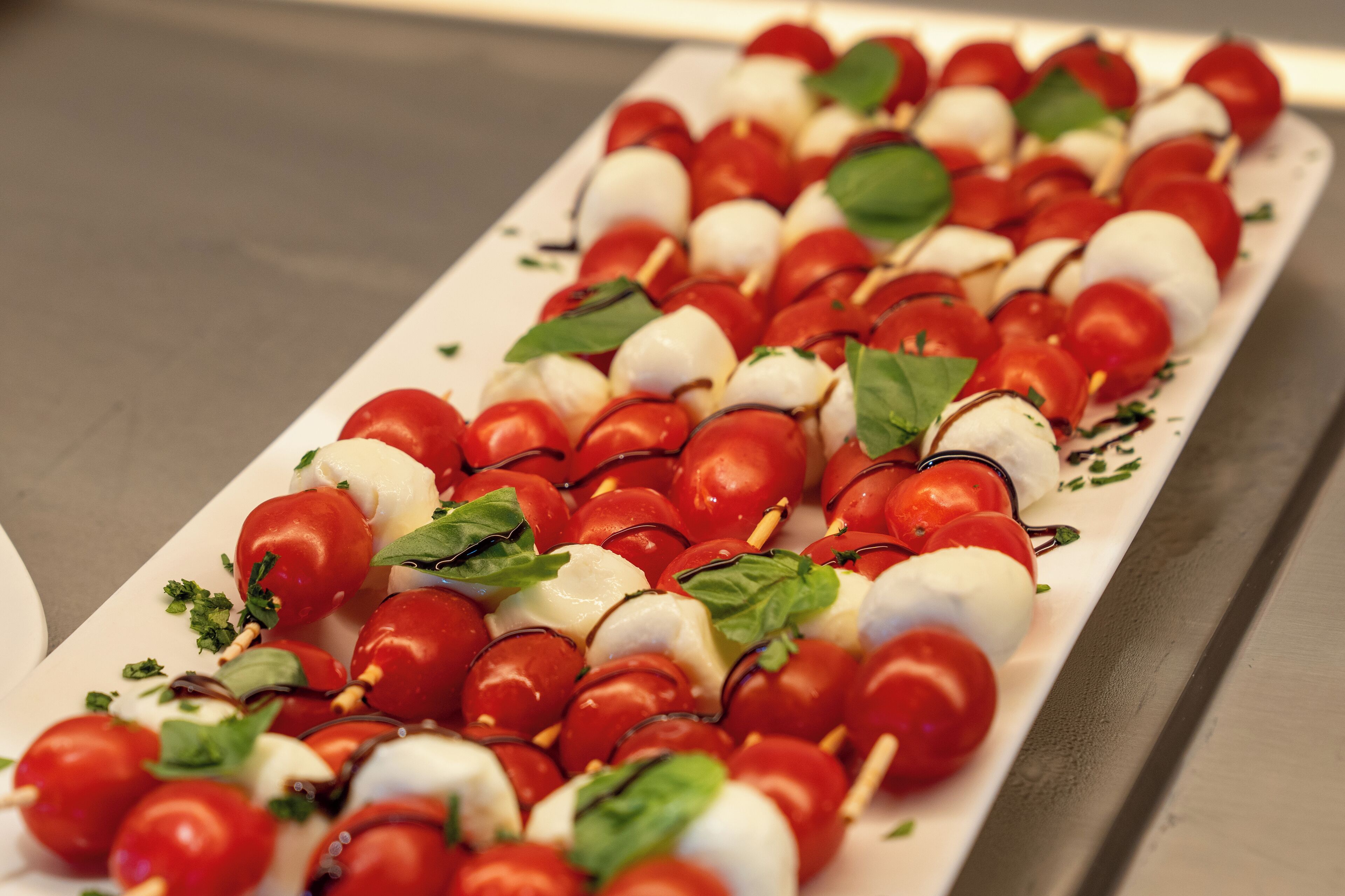 Une assiette de brochettes de mozzarella et de tomates cerises, garnies de basilic.