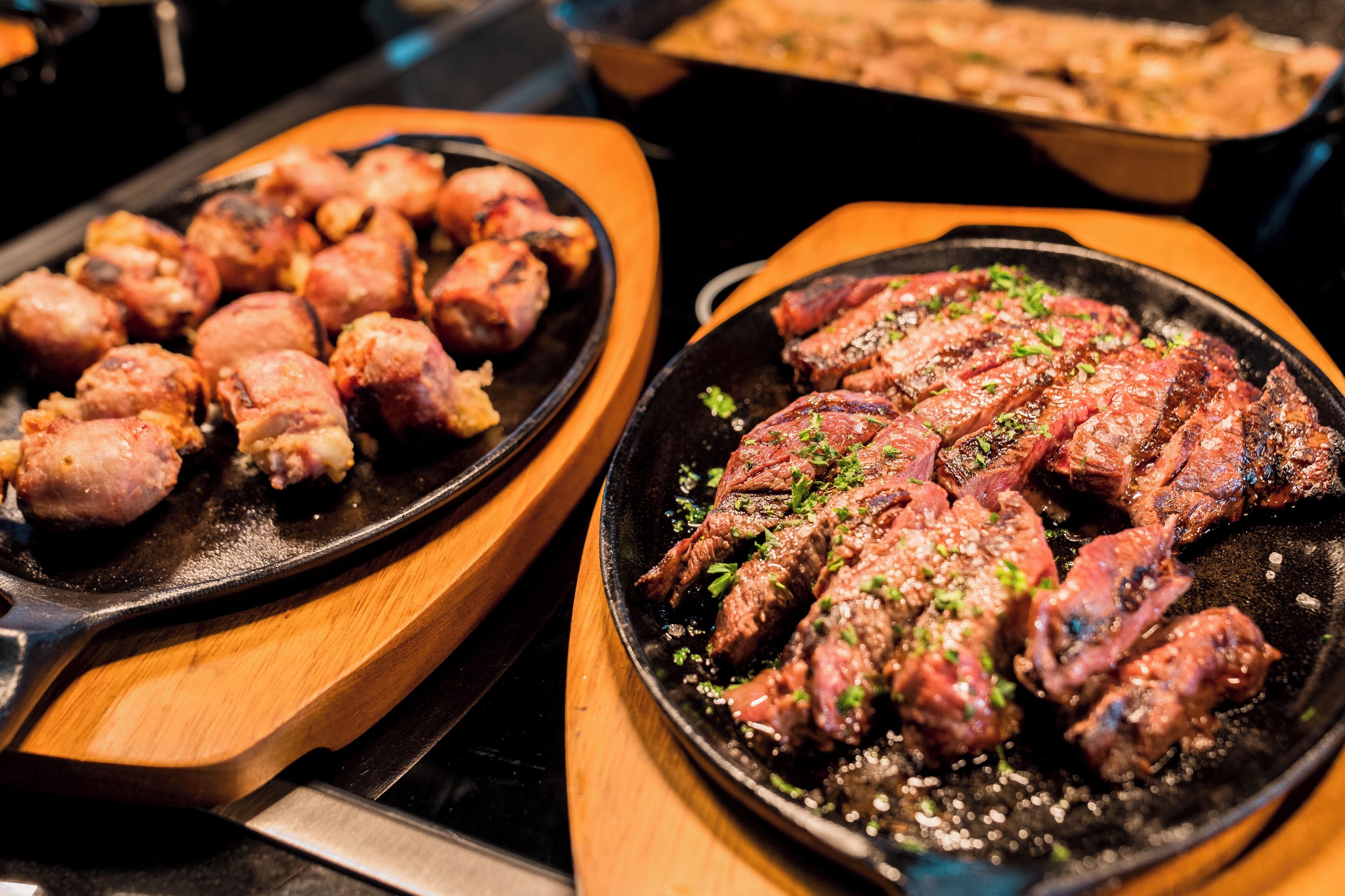 A close-up of grilled meat on a skillet, with a wooden tray and a pan in the background.