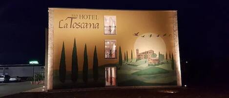 Une grande affiche publicitaire pour l’hôtel I&B La Toscania, sur laquelle on peut voir une fresque représentant un bâtiment, des arbres et des oiseaux.