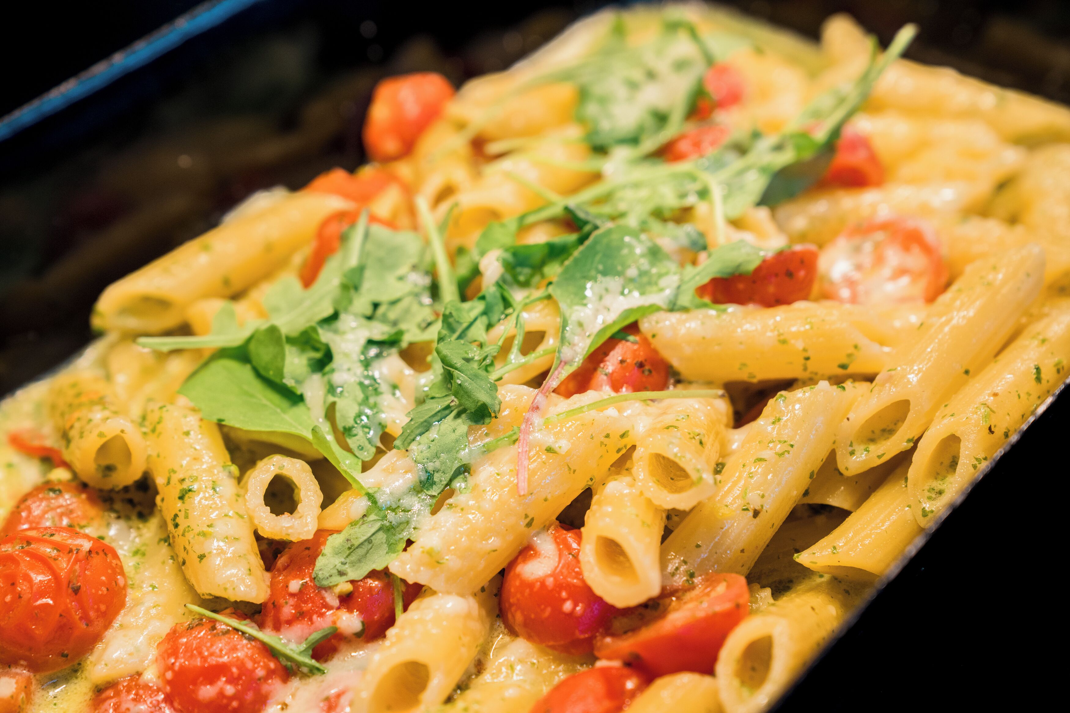 A close-up of a pasta dish with penne, tomatoes, and greens.