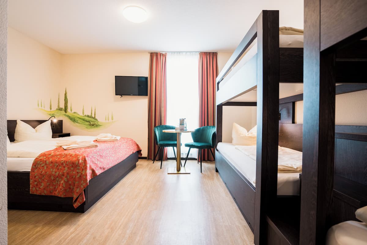 A hotel room with a bed, a desk, two chairs, a TV, and a bunk bed.