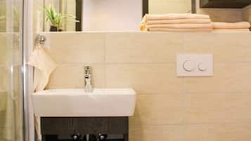 Une salle de bain avec une douche à parois de verre, un lavabo avec un porte-serviettes, des toilettes et une étagère avec des serviettes pliées.