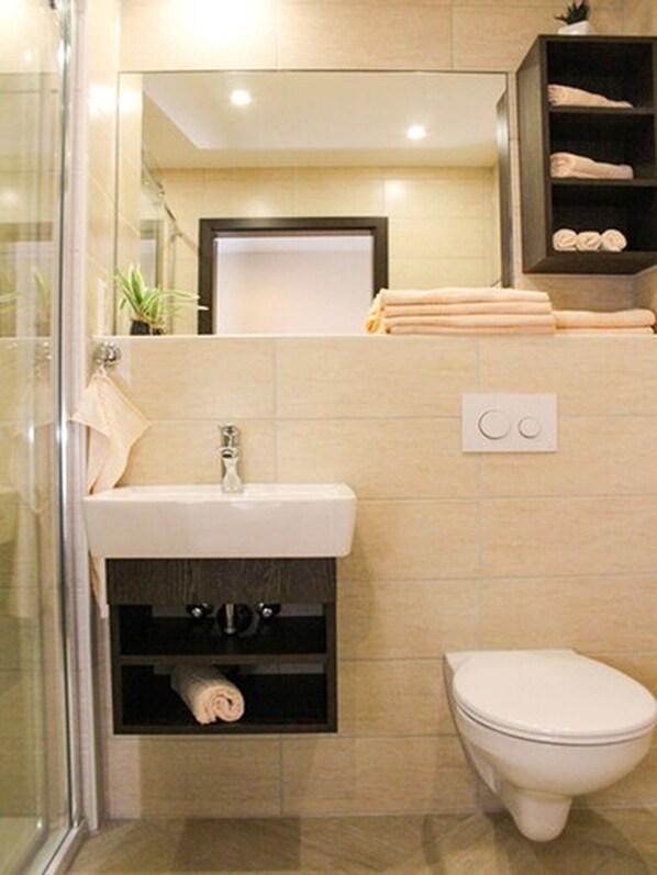 A bathroom with a glass shower enclosure, a sink with a towel rack, a toilet, and a shelf with folded towels. - Hotel La Toscana Nähe Europapark  mit Ticket Garantie (Ringsheim)