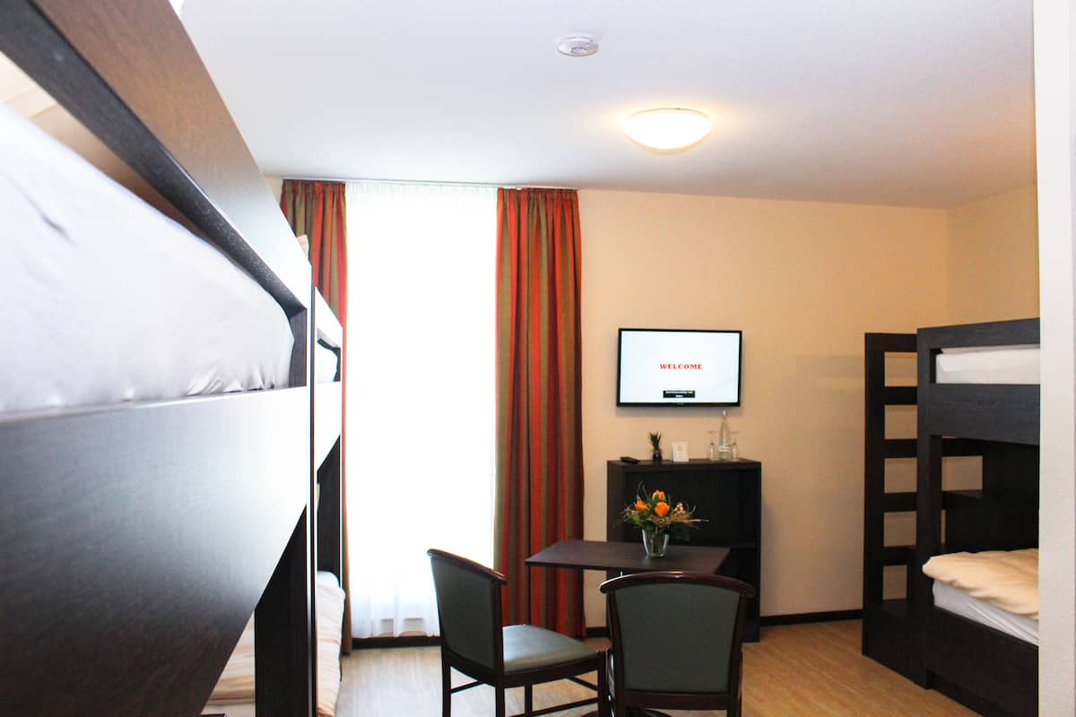 A hotel room with a bunk bed, a desk with a chair, a television, and a window with curtains.