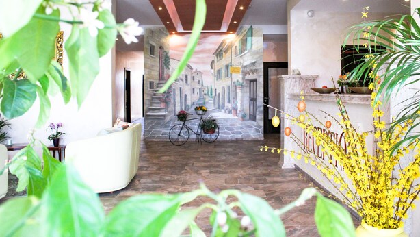 A hotel lobby with a bicycle, potted plants, and a mural of a street scene. - Hotel La Toscana Nähe Europapark  mit Ticket Garantie (Ringsheim)