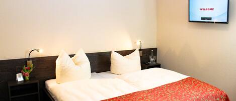 A hotel room with a bed, a TV on the wall, and a nightstand with a lamp.