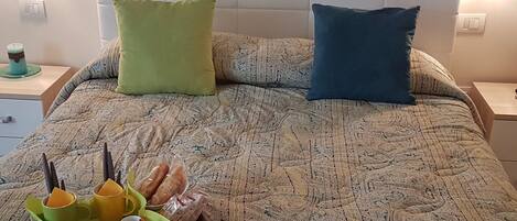 A neatly made bed with a patterned bedspread, two pillows, and a tray with snacks and drinks.