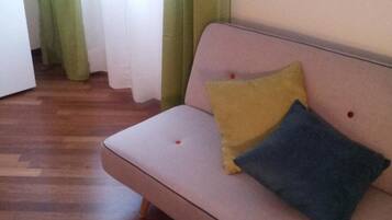 Een kamer met een bank, groene gordijnen en een houten vloer.
