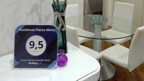 A modern room with a glass table and chairs, a decorative vase with plants, and a framed award plaque. - B&B Residenza Piazza Moro (Bari)