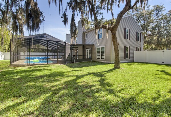 A house with a covered patio, a swimming pool, and a well-maintained lawn.