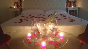 A bed with rose petals and candles, a bottle of champagne, and two glasses on a glass table. - Dimora San Biagio Suites & Apartment (Lecce)