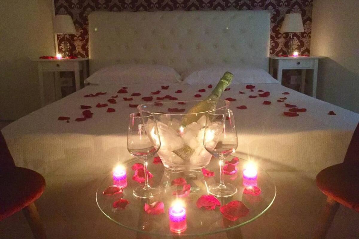 Ein Bett mit Rosenblättern und Kerzen, eine Champagnerflasche und zwei Gläser auf einem Glastisch.