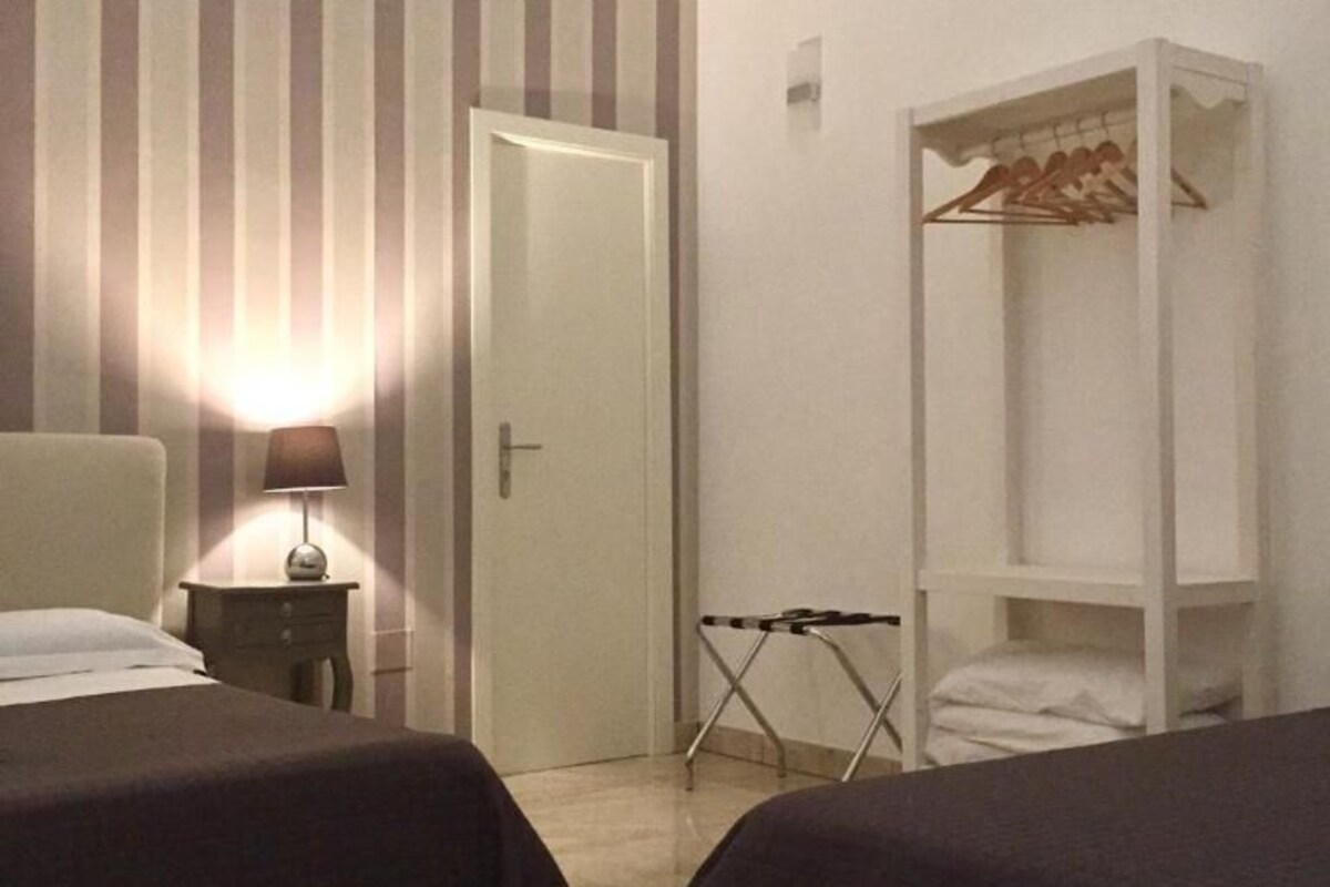 Camera d'albergo con due letti, un comodino con una lampada, un armadio e una parete a righe.