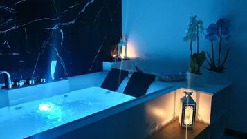 Un baño moderno con pared de mármol, una bañera, un lavabo y una pequeña mesa con objetos decorativos.