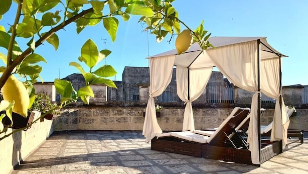 A rooftop terrace with a canopy bed, stone flooring, and a view of buildings in the background. - Dimora San Biagio Suites & Apartment (Lecce)