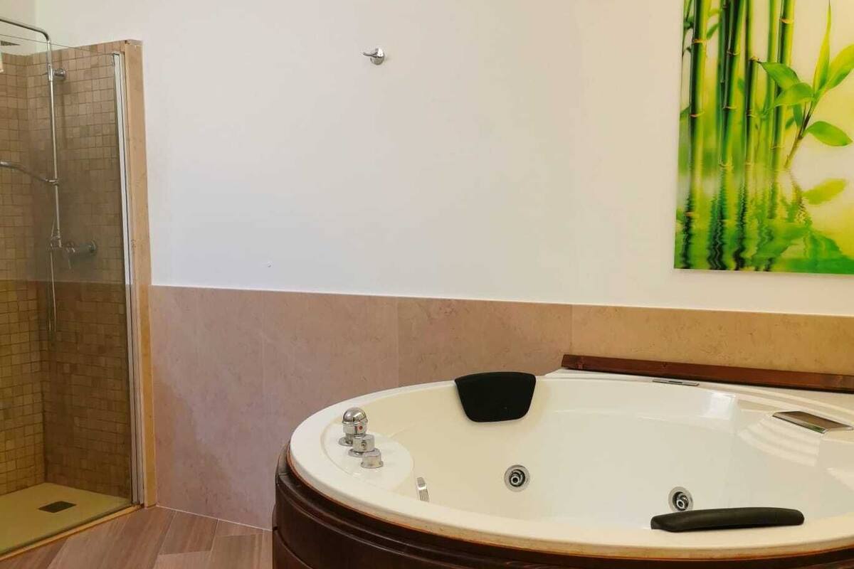 Ein Badezimmer mit einer gläsernen Duschkabine, einer Holzbade Wanne und einer Wandmalerei mit Bambus-Motiv.