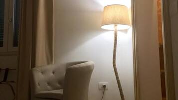 A hotel room with a bed, a chair, a floor lamp, and a door leading to another room.