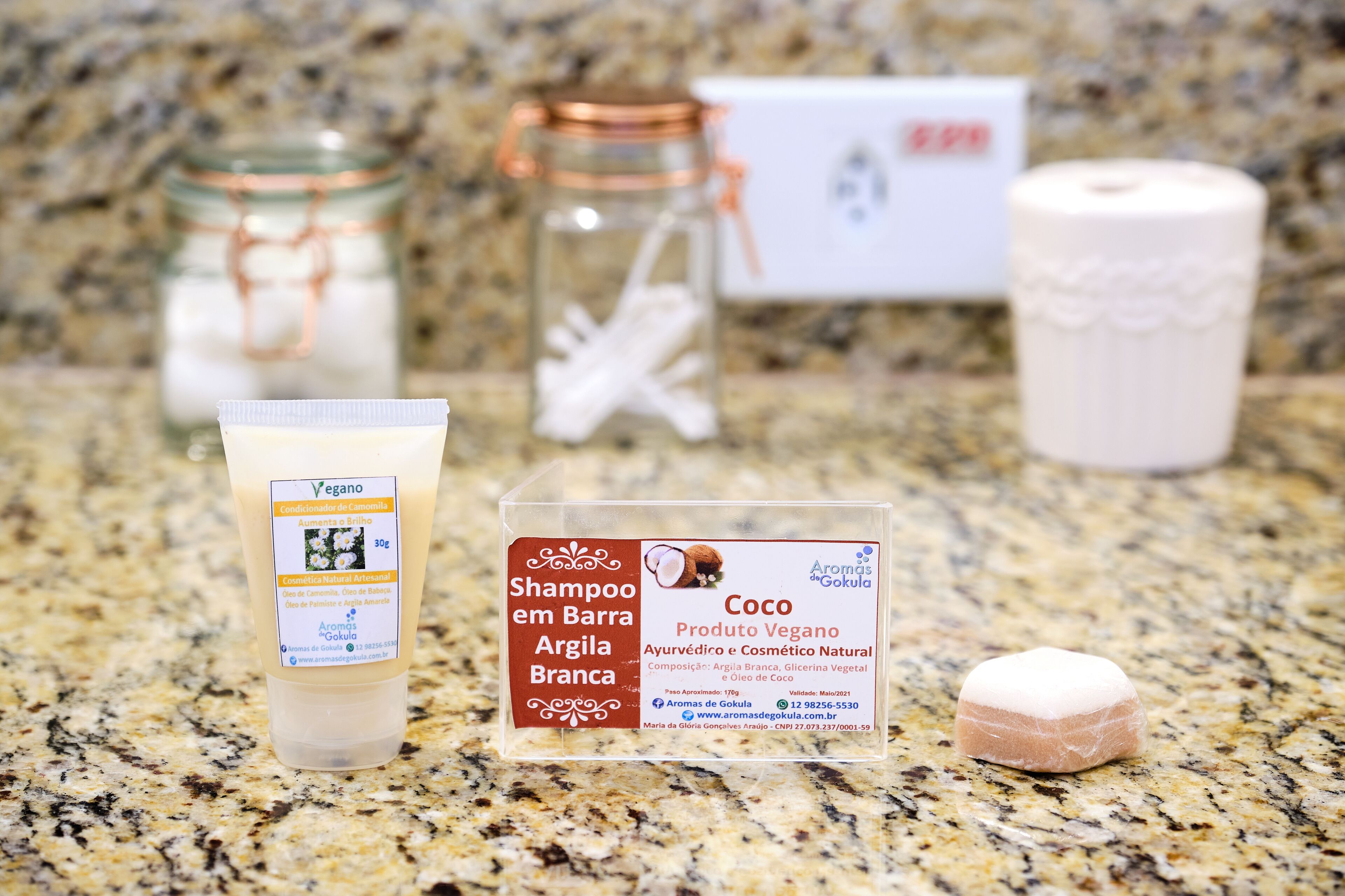 A product display with a shampoo bottle, a jar, a candle, and a box on a granite countertop.
