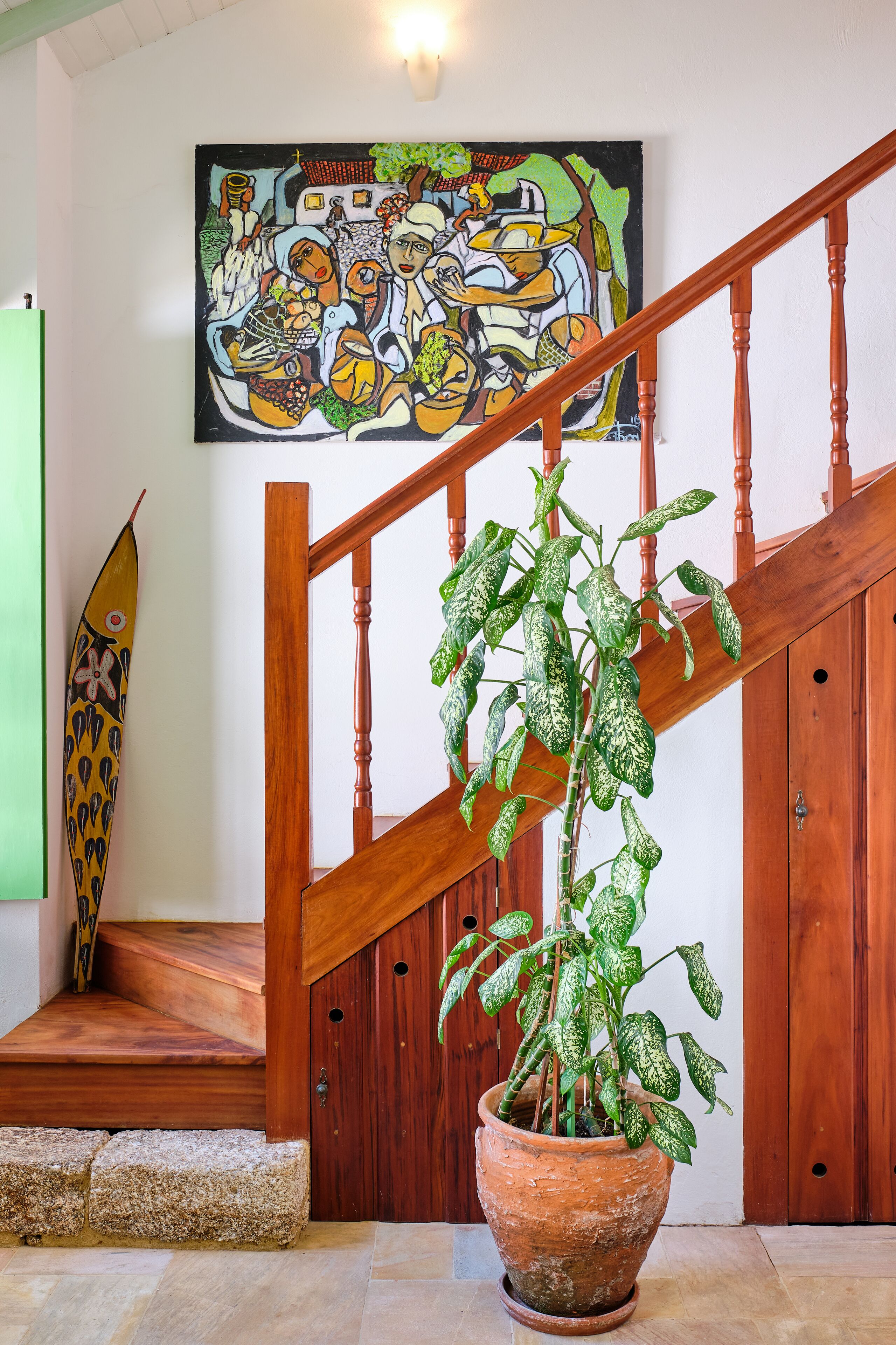 A staircase with a wooden handrail, a potted plant with variegated leaves, and a colorful painting on the wall.