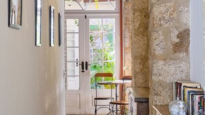 A hallway with a patterned rug, a wooden bench, a stone wall, and a bookshelf with books and a glass object. - A Casa de Paulo Autran (Paraty)