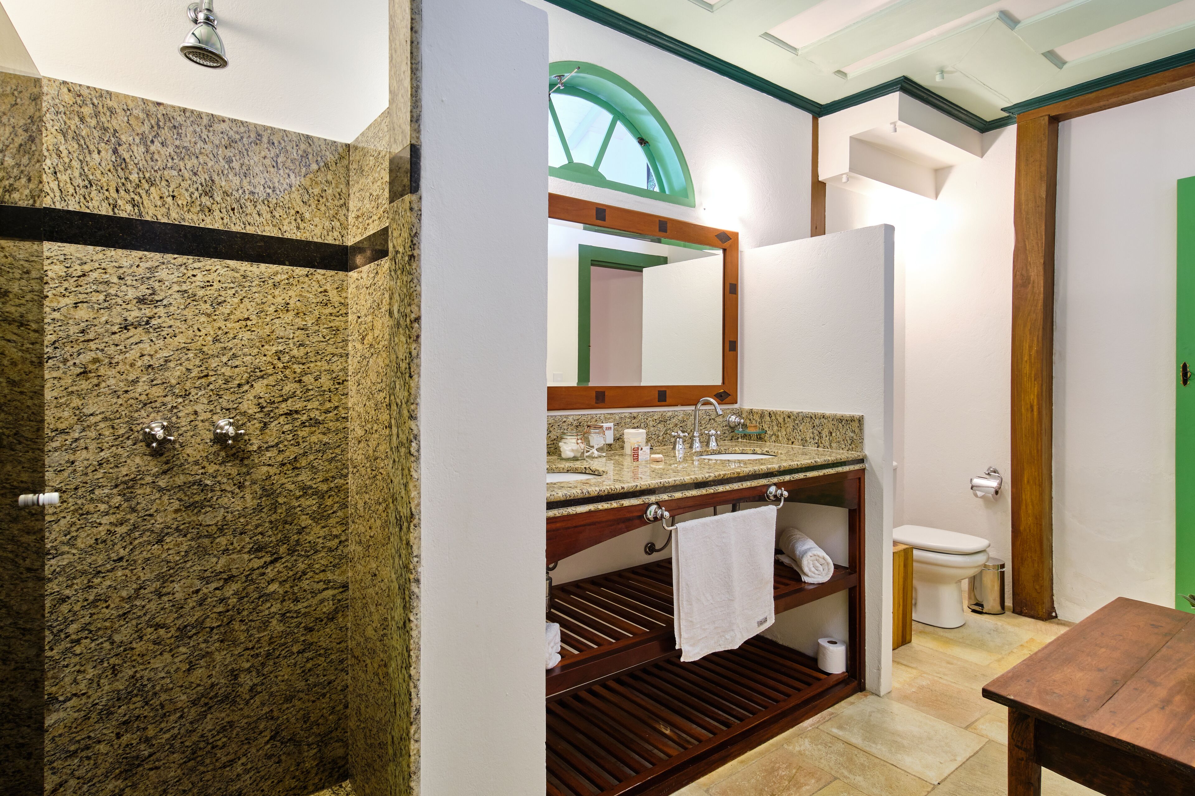 Un baño con lavamanos de encimera de granito, un espejo, un inodoro y un mueble de tocador de madera.