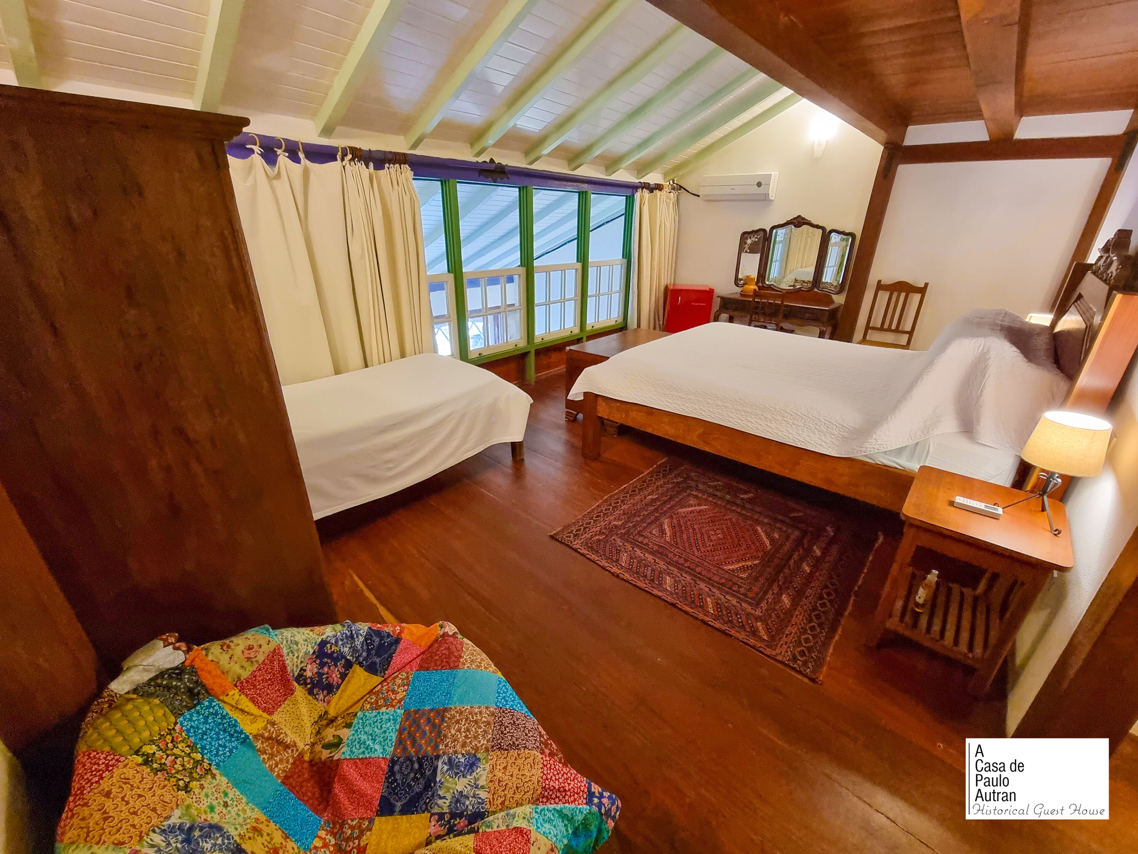 Een slaapkamer met twee bedden, een houten vloer, een kleurrijk sprei en een raam met gordijnen.