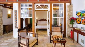 A spacious room with a large wooden bed, two chairs, a chess table, and a painting on the wall. - A Casa de Paulo Autran (Paraty)