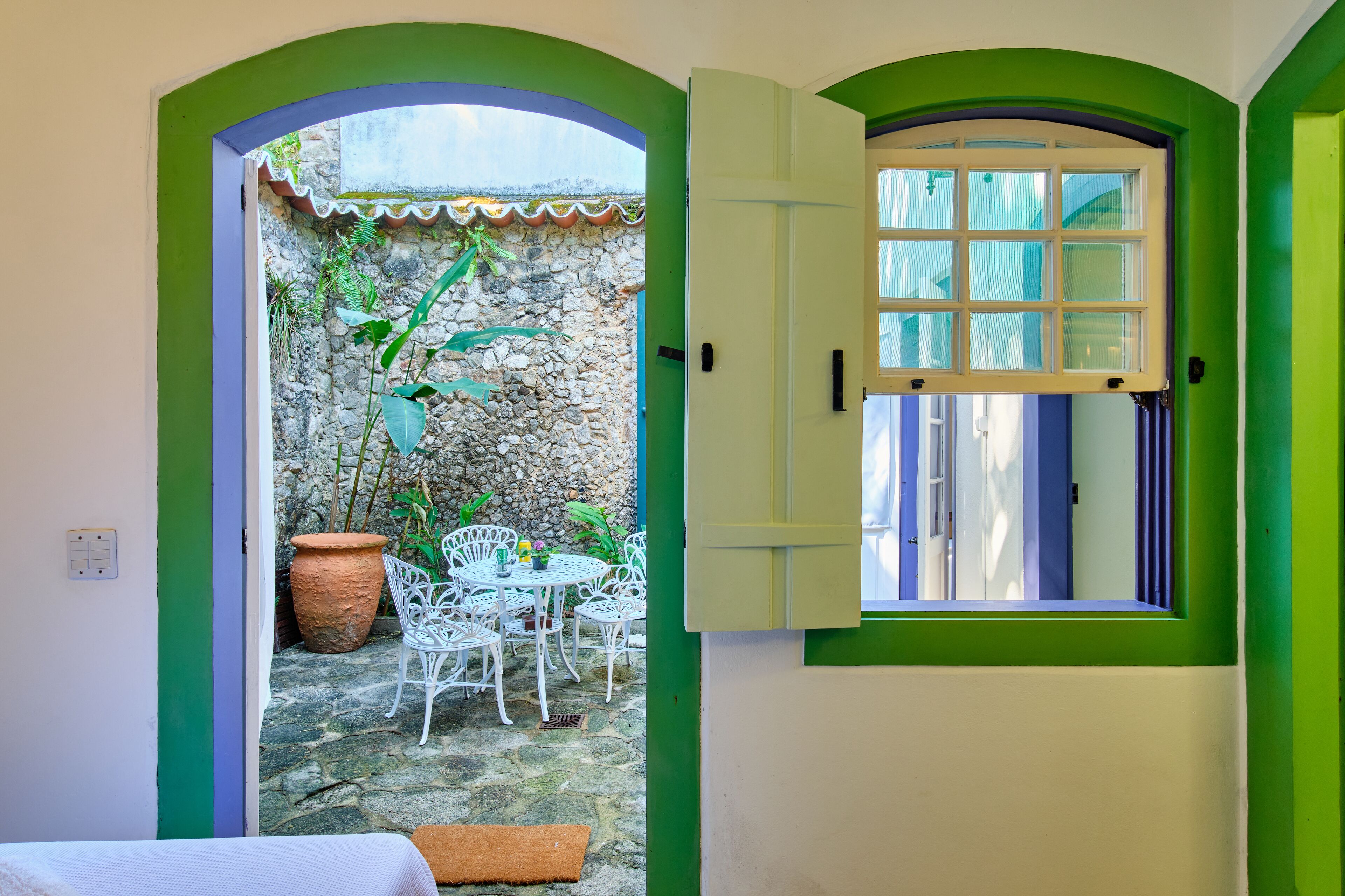 A room with a stone wall, a window with blue shutters, and a white chair outside.