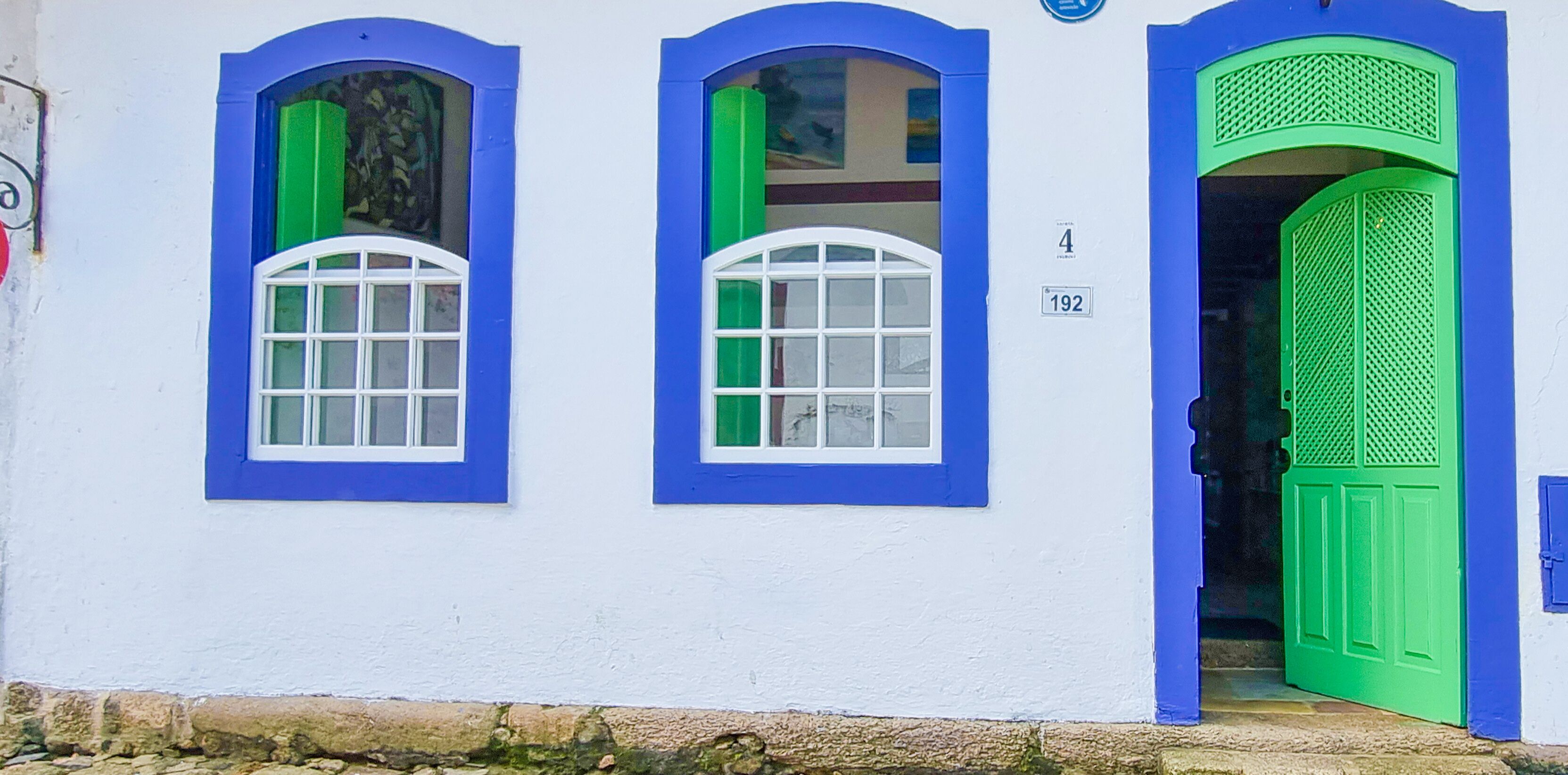 A building with three arched windows, each with a white frame and blue trim. The building number is 192, and there is a green door with a lattice design.
