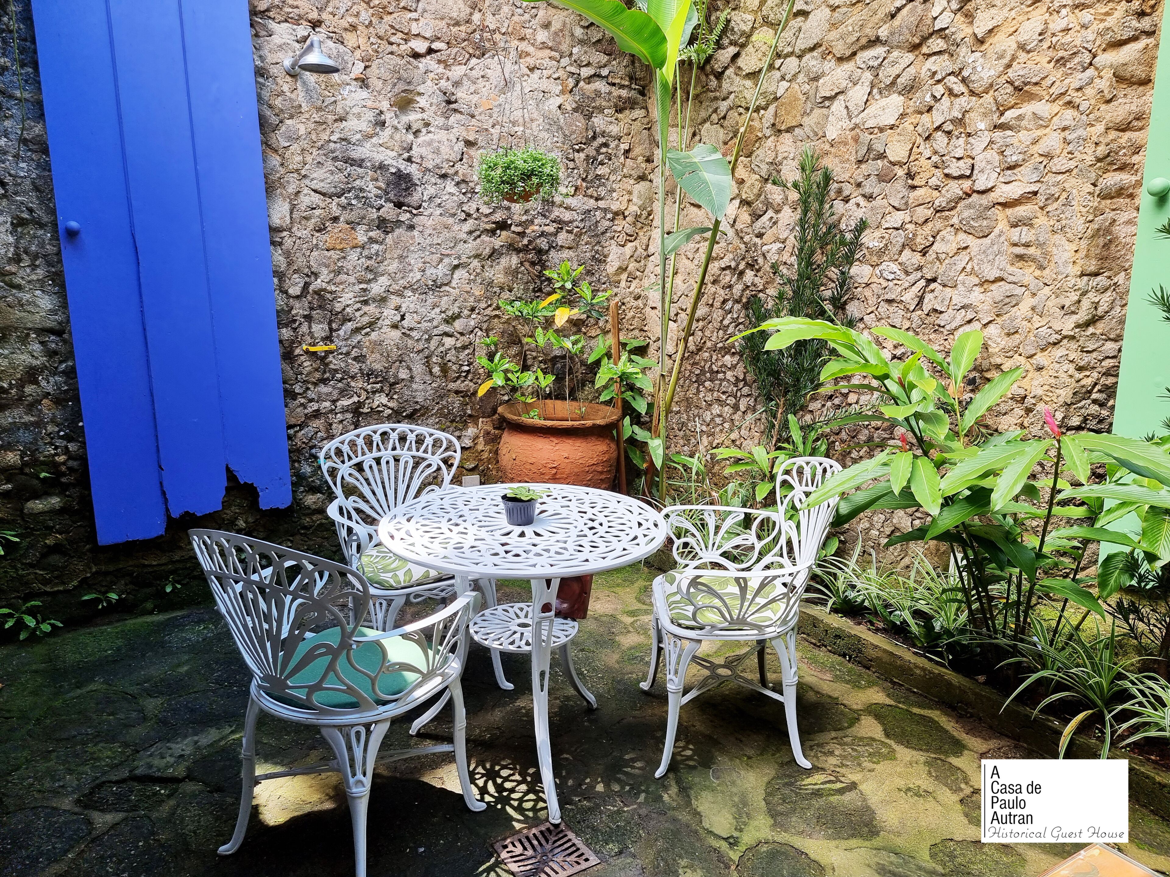 A patio with white metal chairs and a table, a blue door, and a stone wall.