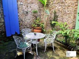 Een terras met witte metalen stoelen en een tafel, een blauwe deur en een stenen muur.