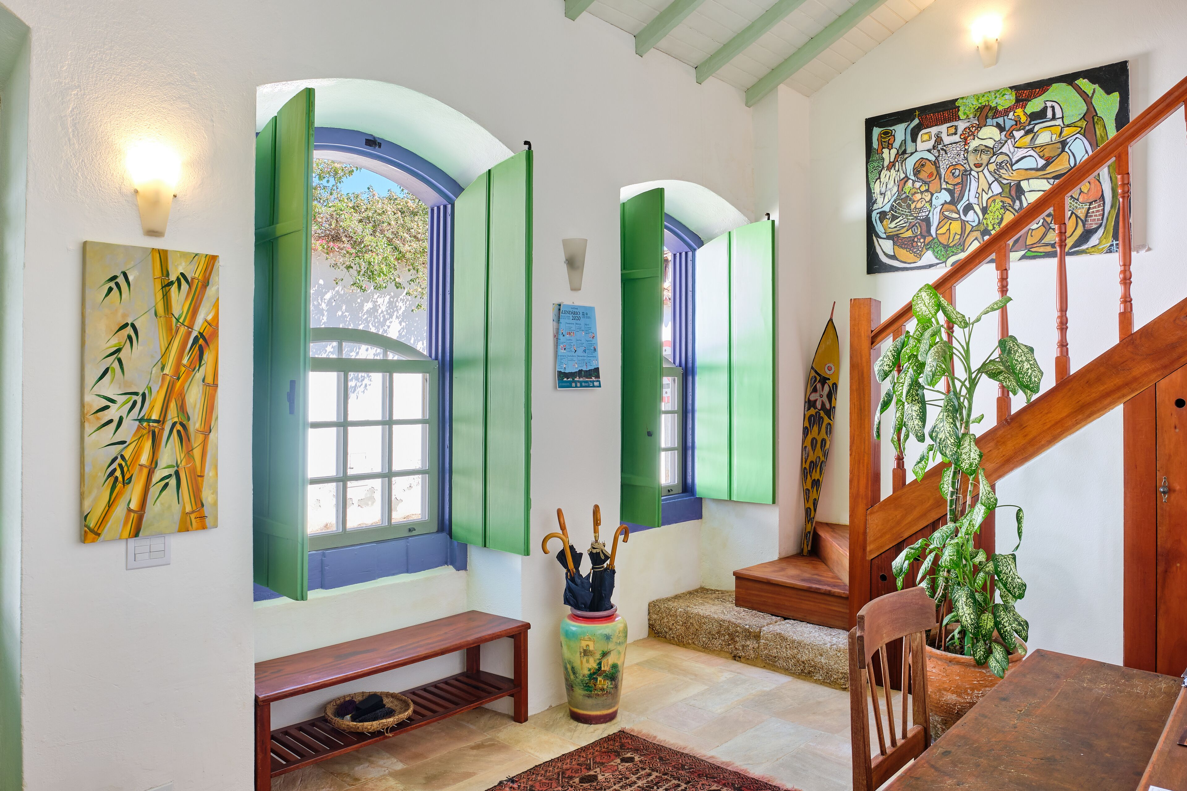 A room with a wooden staircase, a large painting, and a vase with umbrellas.