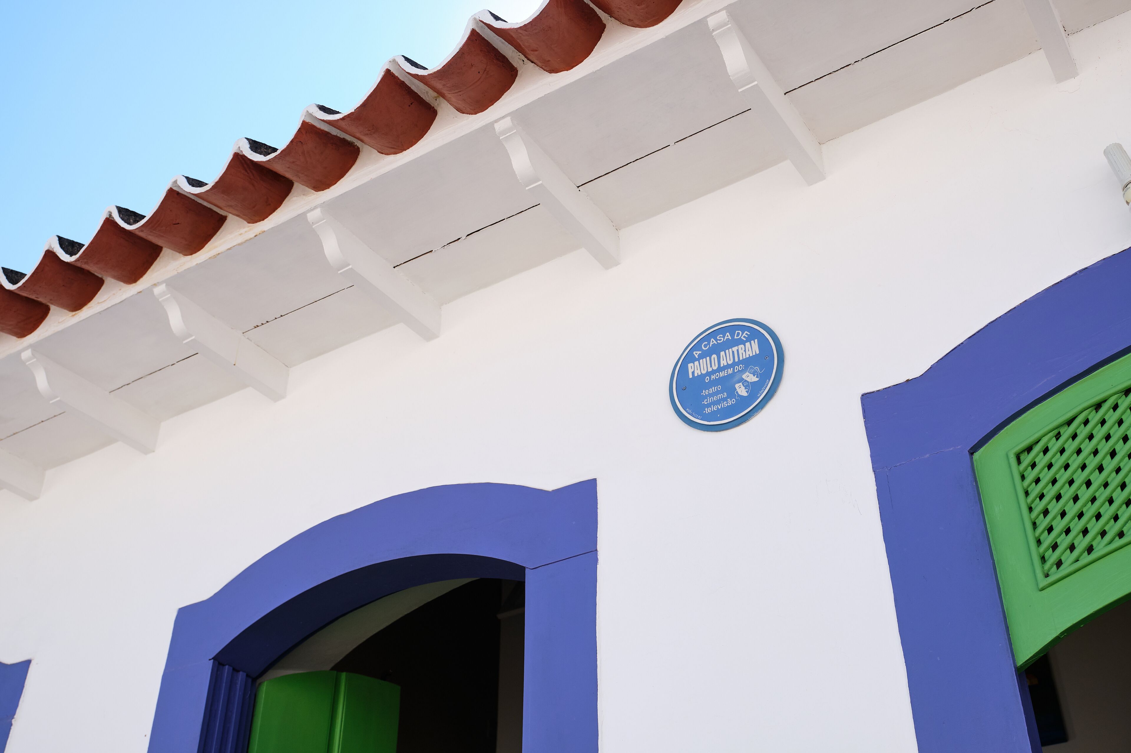 Un bâtiment à la façade bleue et blanche, avec une enseigne bleue indiquant la présence d’une salle de télévision, et un cadre de fenêtre vert.