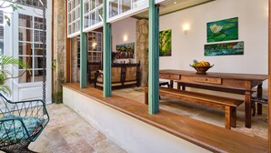 A dining area with a wooden table, benches, and a hanging chair. There are paintings on the wall and a window with a view of the outdoors. - A Casa de Paulo Autran (Paraty)