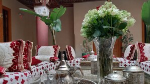 A traditional Moroccan interior with patterned sofas, a decorative tray with silverware, a brass water pitcher, and a floral vase. - Riad Miral (Marrakech)
